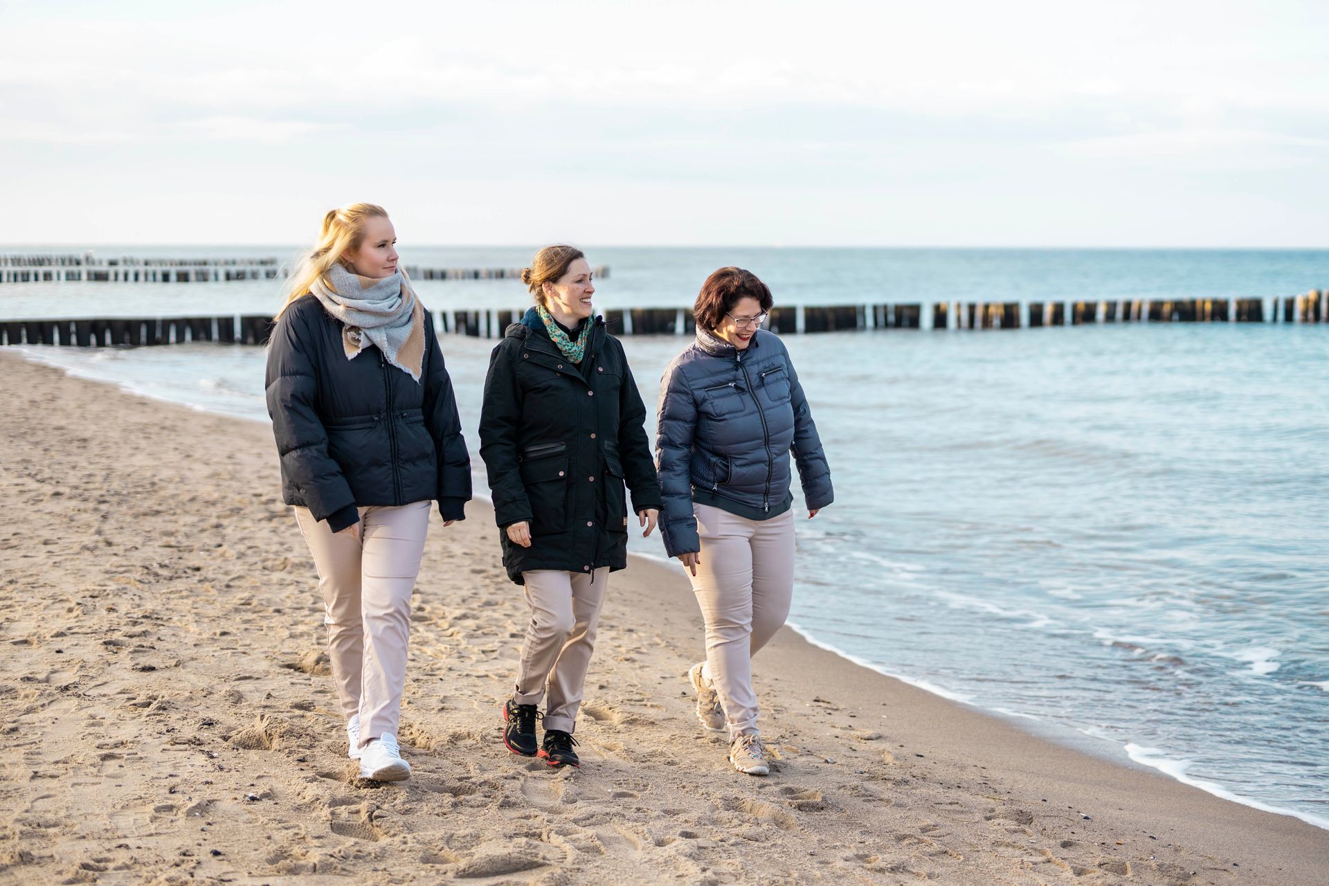 Drei Frauen gehen am Strand in der Nähe des Meeres spazieren.