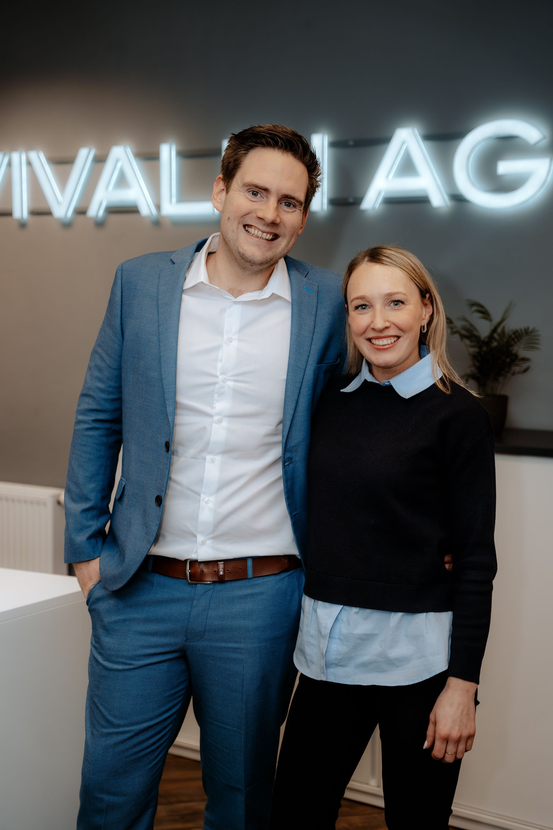 Eine Frau sitzt lächelnd an einem Schreibtisch vor einem Fenster.