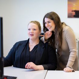 Zwei Frauen schauen auf einen Computerbildschirm und lächeln