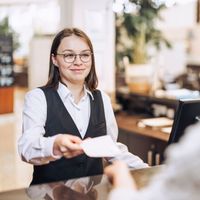 Eine Frau gibt einer anderen Person an einem Schalter ein Stück Papier.