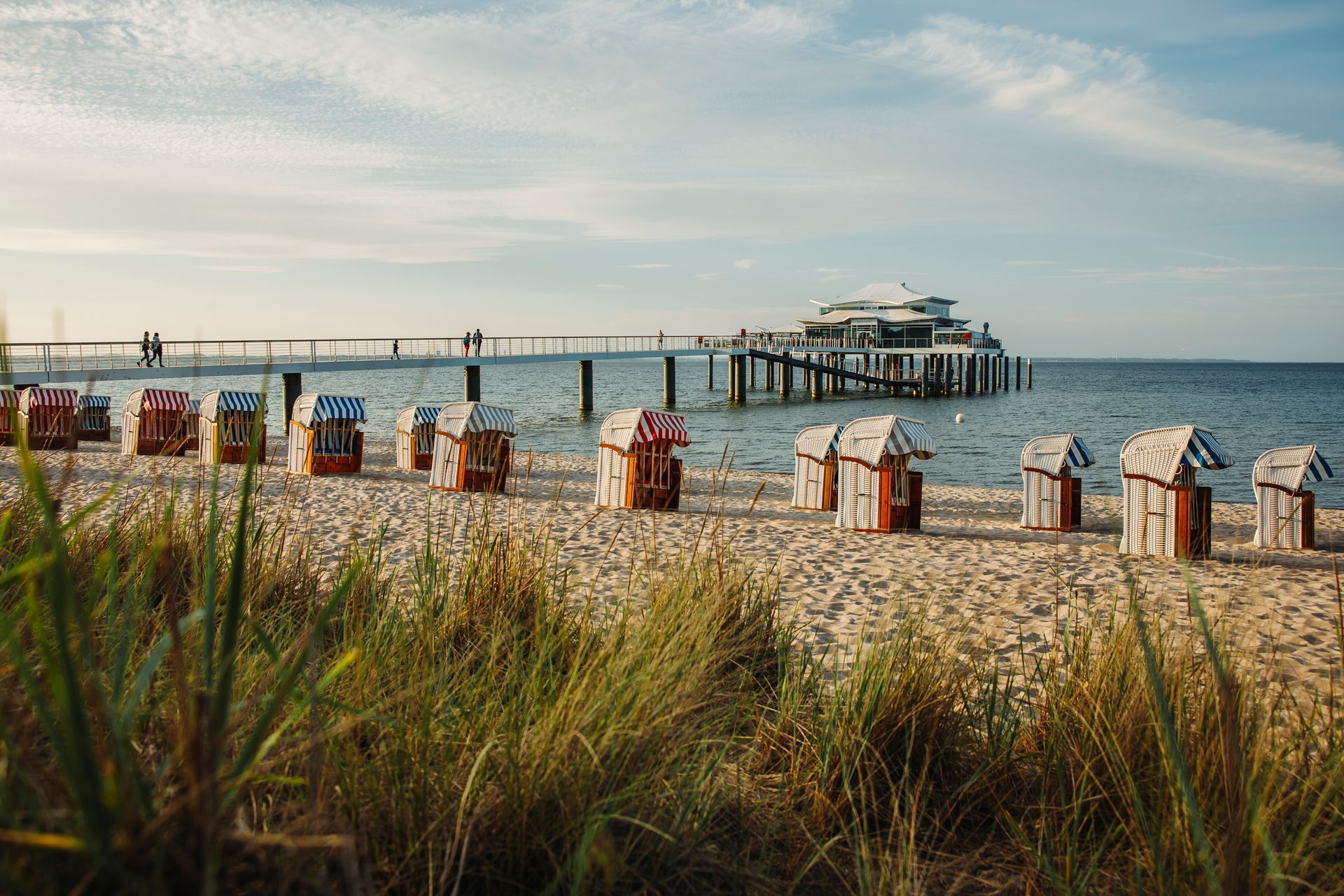 Eine Reihe von Strandstühlen an einem Strand mit einem Pier im Hintergrund.