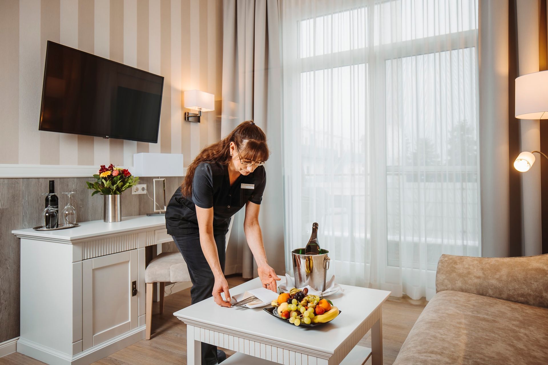 Ein Hotelzimmer mit einem Mitarbeiter, der einen Tisch mit Obst und Champagner deckt