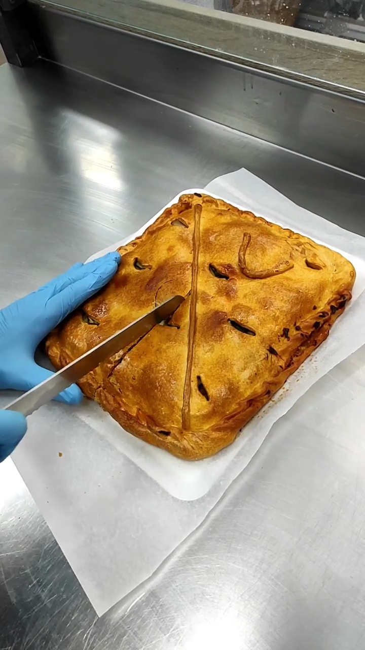 Una mano enguantada corta un pastel dorado sobre papel pergamino.