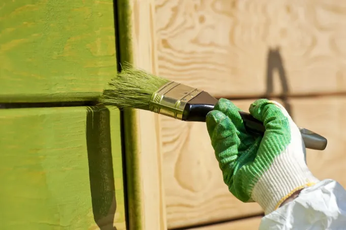 Mano con guante verde pintando con pintura verde una estructura de madera.