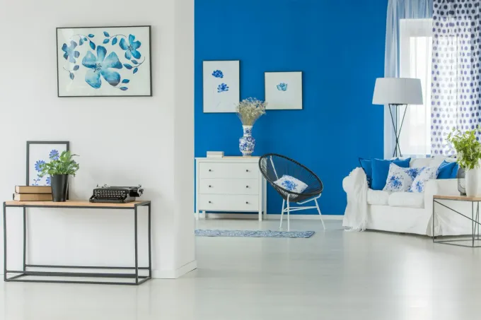 Salón azul brillante y blanco; un sofá y paredes blancas contrastan con una pared decorativa azul y obras de arte.