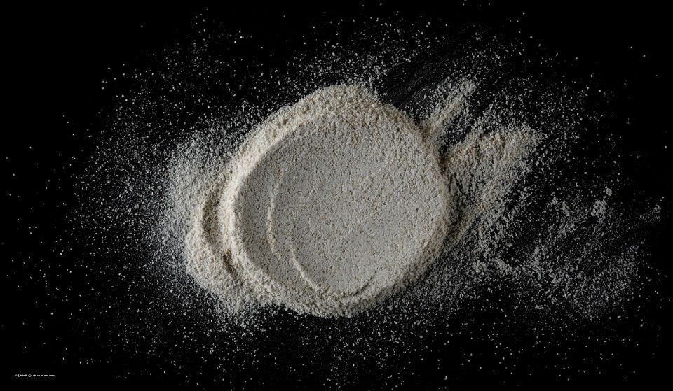 Ein Haufen weißes Mehl auf schwarzem Untergrund; Mehlreste an den Rändern.