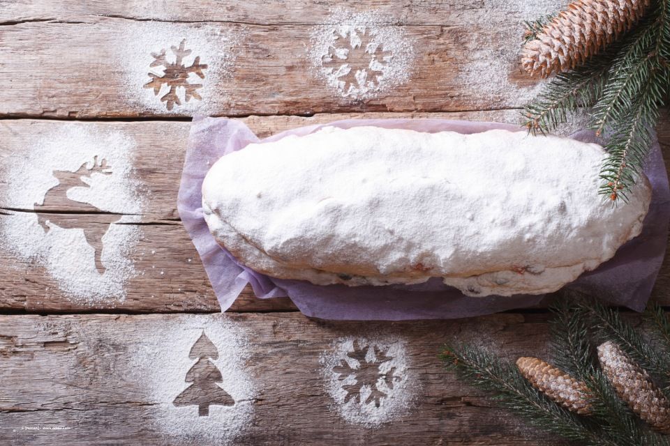 Stollenbrot, mit Puderzucker bestäubt, auf einer mit weihnachtlichen Schablonen verzierten Holzoberfläche.