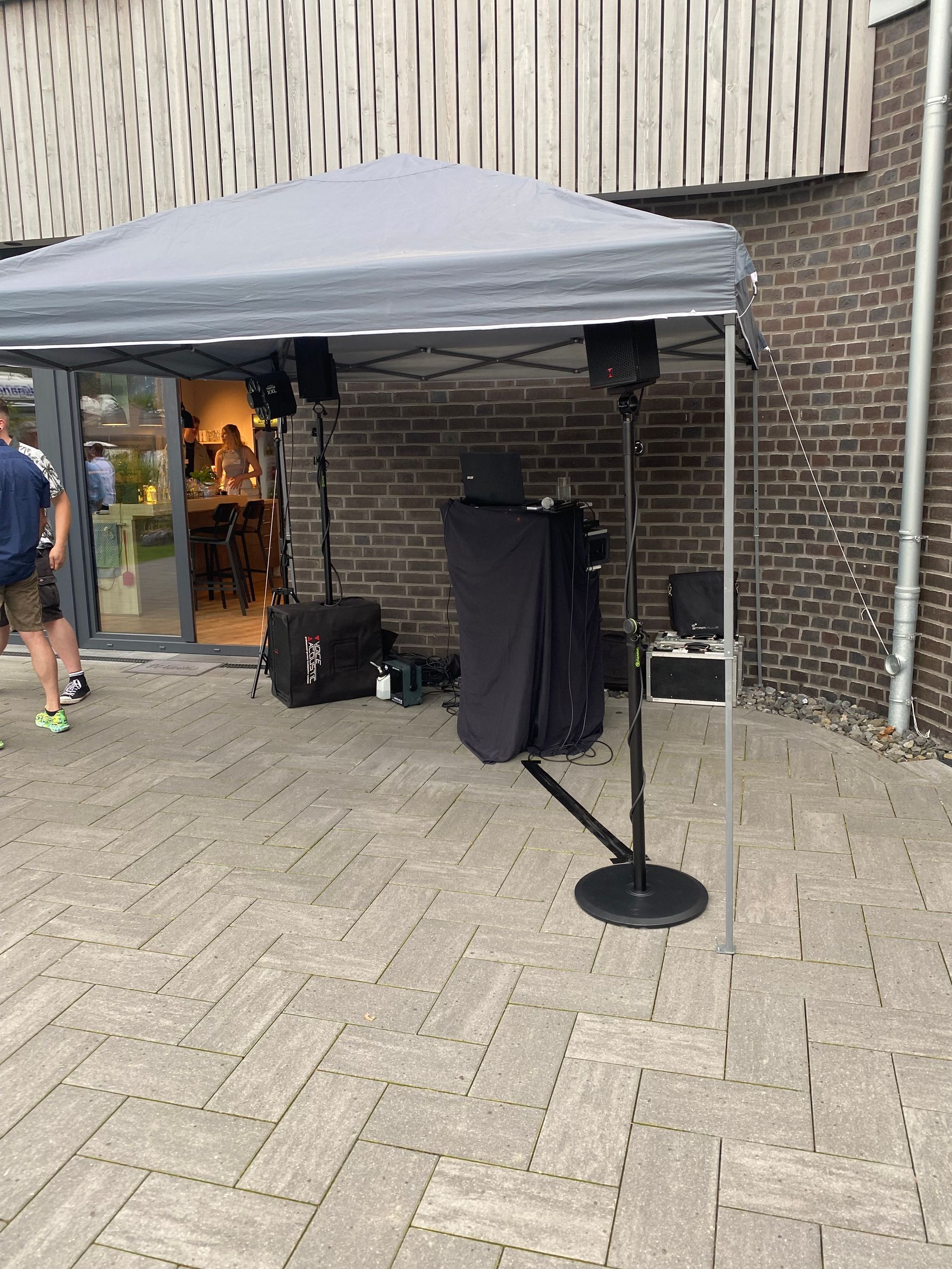 Ein Mann geht an einem Zelt mit Lautsprechern und einem Mikrofon vor einem Backsteingebäude vorbei.