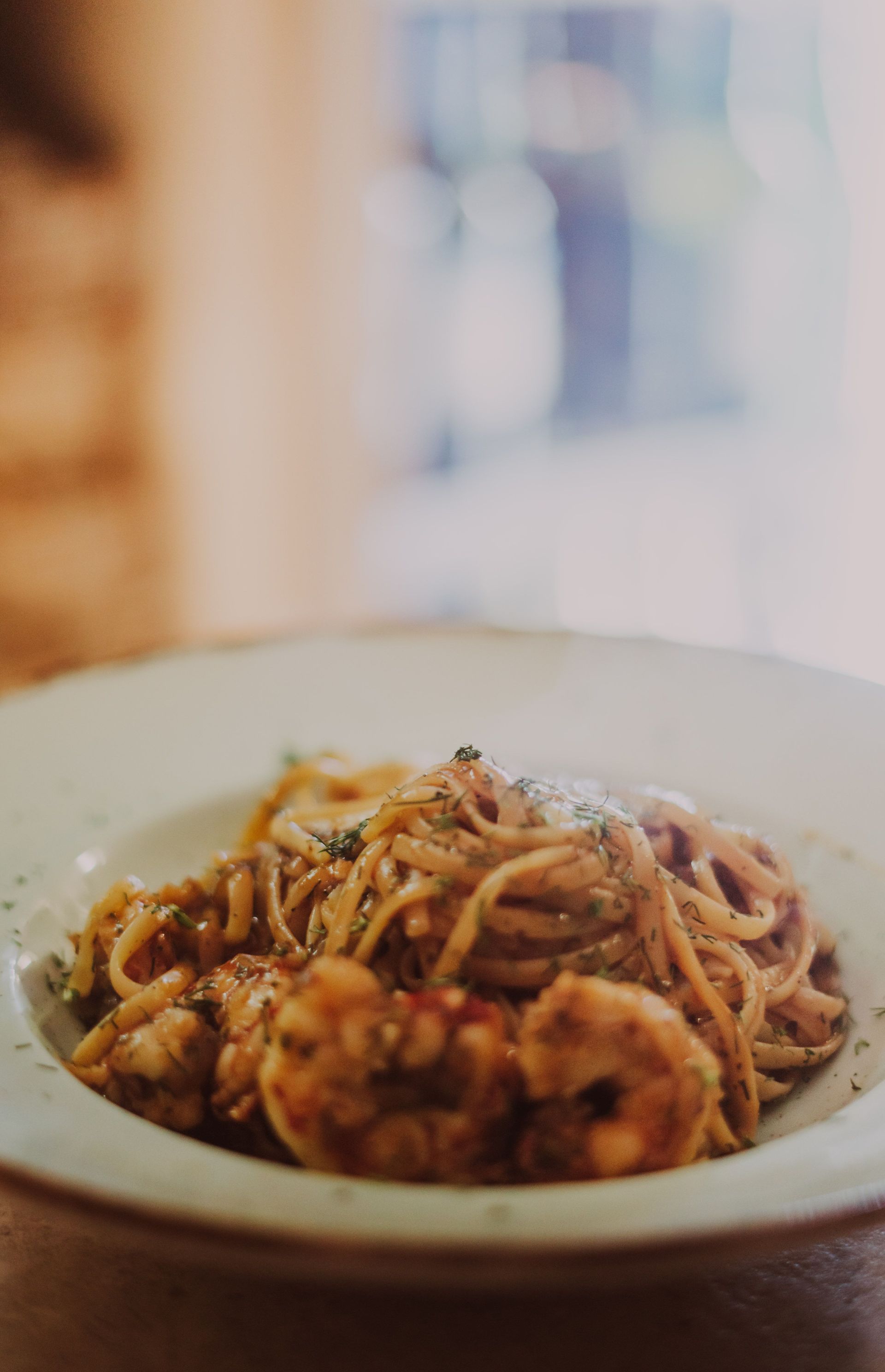 Menschen geniessen gemeinsam ein Pastagericht mit Wein und Tomaten an einem warm beleuchteten Tisch.