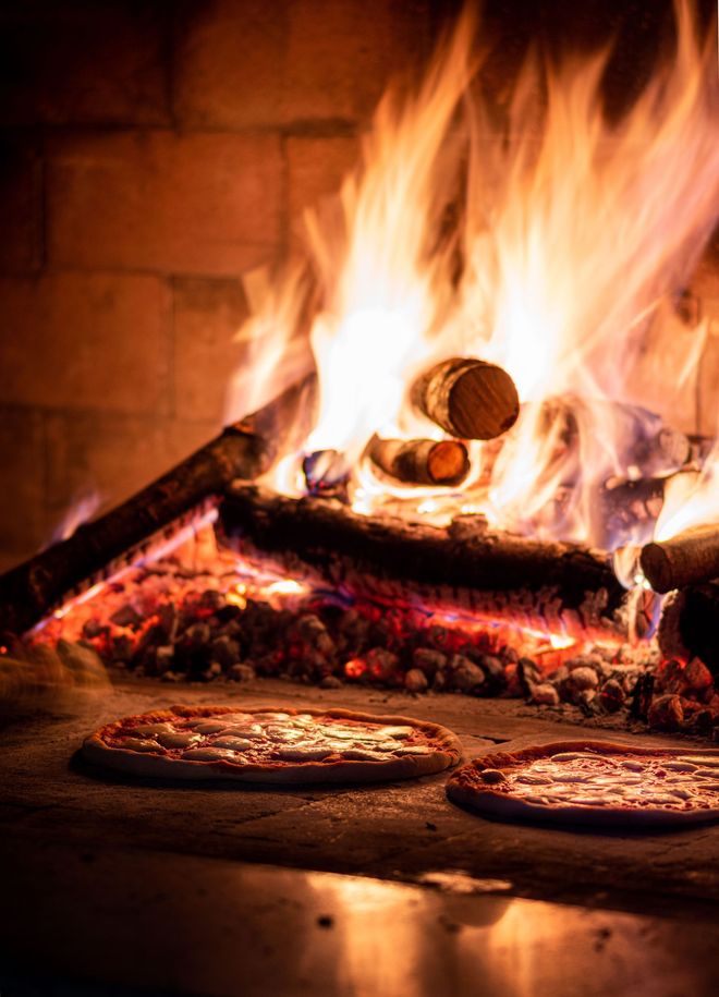 Hände heben Weingläser über einem Tisch voller Pizza und Pasta während eines gemeinsamen Essens