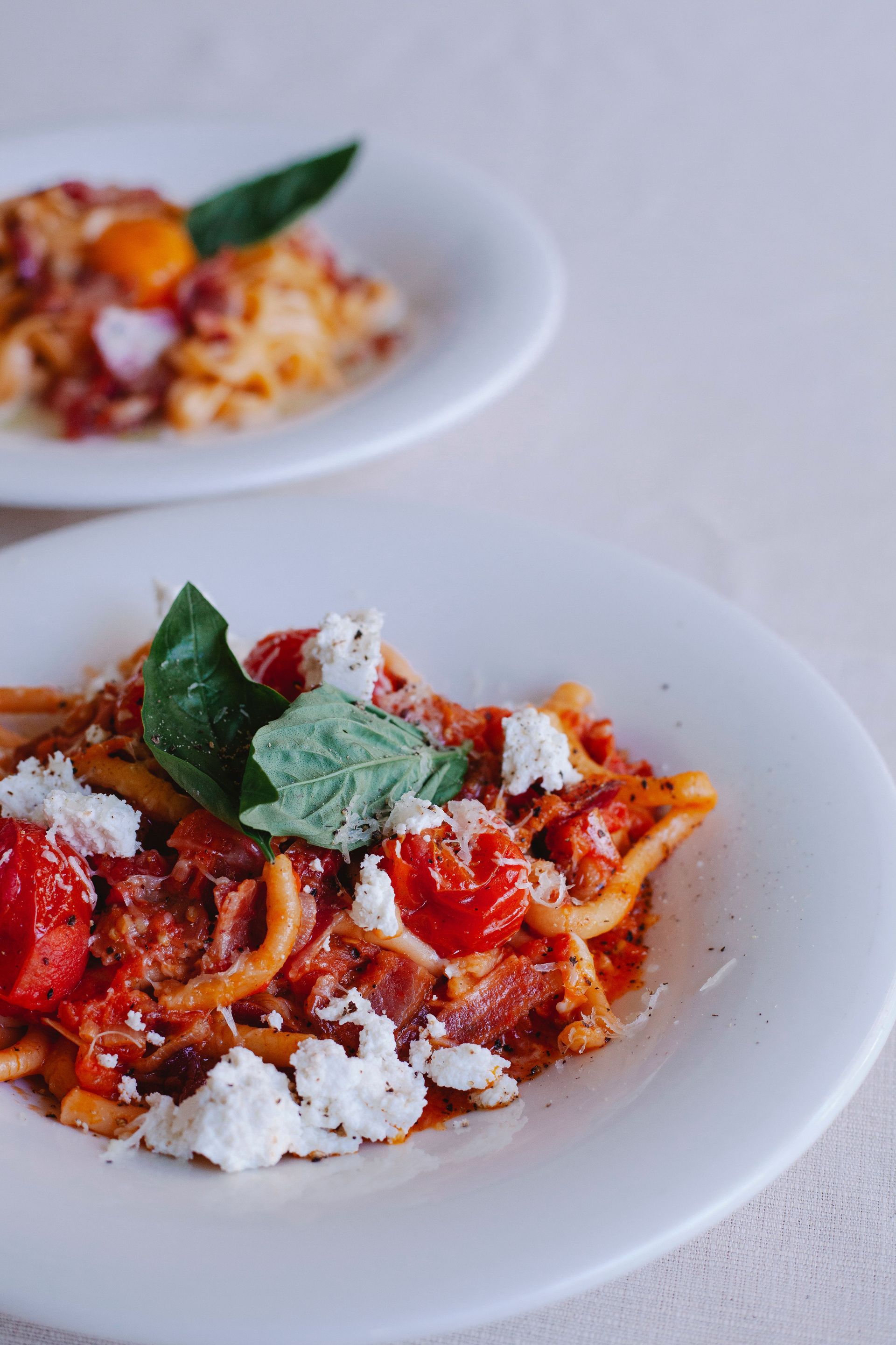 Ein Teller Spaghetti mit Kräutern und Käse, serviert in einem Restaurant mit Weingläsern im Hintergrund.