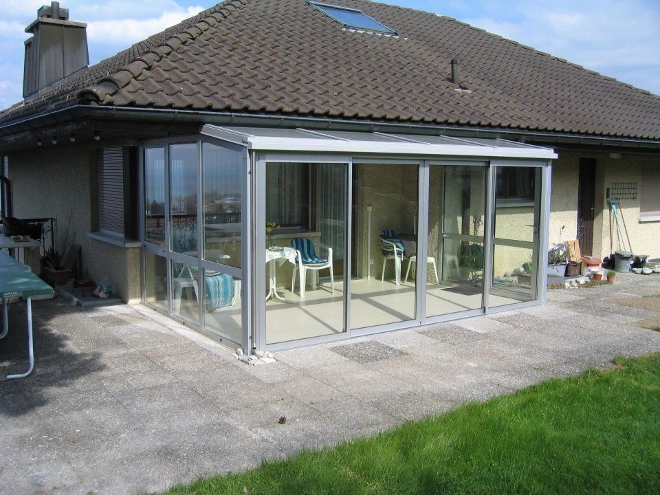 Rückseite eines Hauses mit verglaster Terrasse und Ziegeldach, vom Hof aus betrachtet.