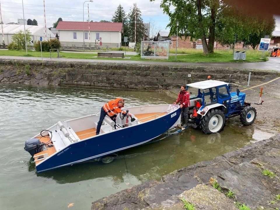 Arbeiter laden ein blaues Boot von einem Traktor in einen Kanal.
