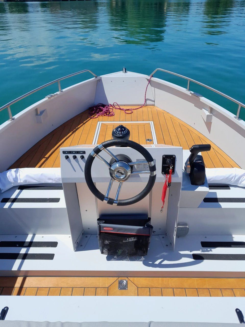 Bootsbug mit Steuerrad und Konsole, der vom Deck aus auf ruhiges blaues Wasser gerichtet ist.