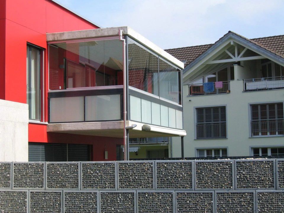 Moderne Wohnungsbalkone hinter einer gemusterten Sichtschutzwand, mit einer rot-weissen Gebäudefassade