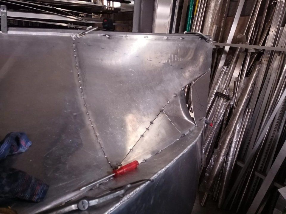Beschädigtes Metallblech, in dessen geknickter Industrieoberfläche ein Werkzeug mit rotem Griff steckt.