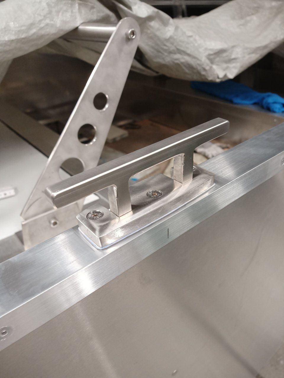 Nahaufnahme eines silbernen Metallverschlusses mit Scharnier, der auf einer gebürsteten Aluminiumoberfläche montiert ist.