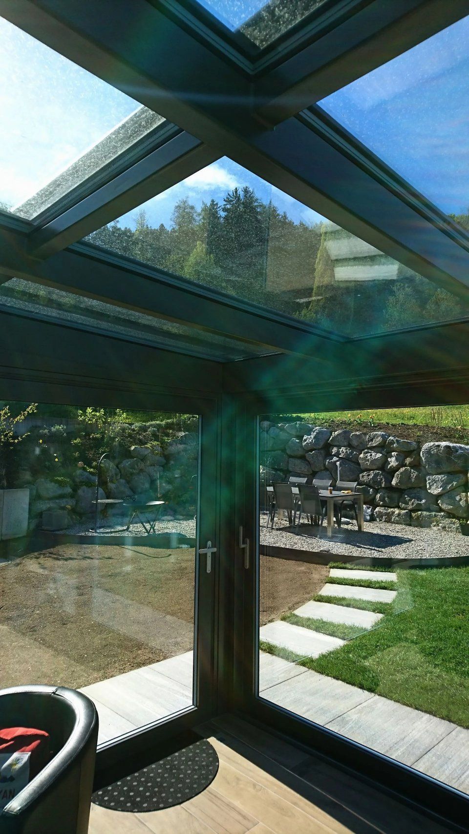 Lichtdurchfluteter Wintergarten mit Glasfront und Blick auf einen Garten mit Rasen, Steintreppe und Stützmauer