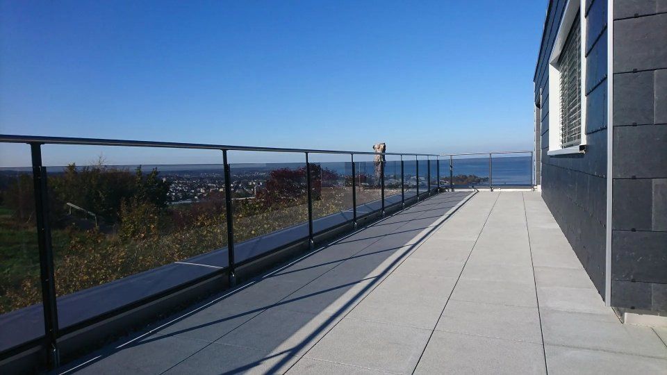 Sonnendurchflutete Dachterrasse mit Glasgeländer, Fliesenboden und Meerblick