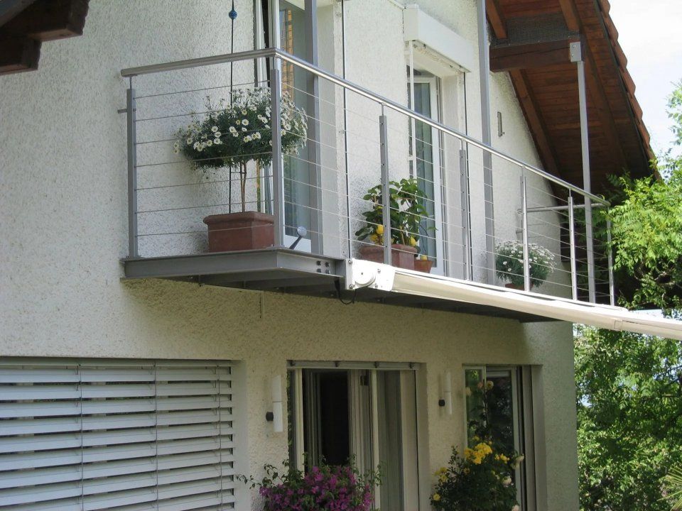 Moderner Hausbalkon mit Glasgeländer und Topfblumen über einem Fensterladen