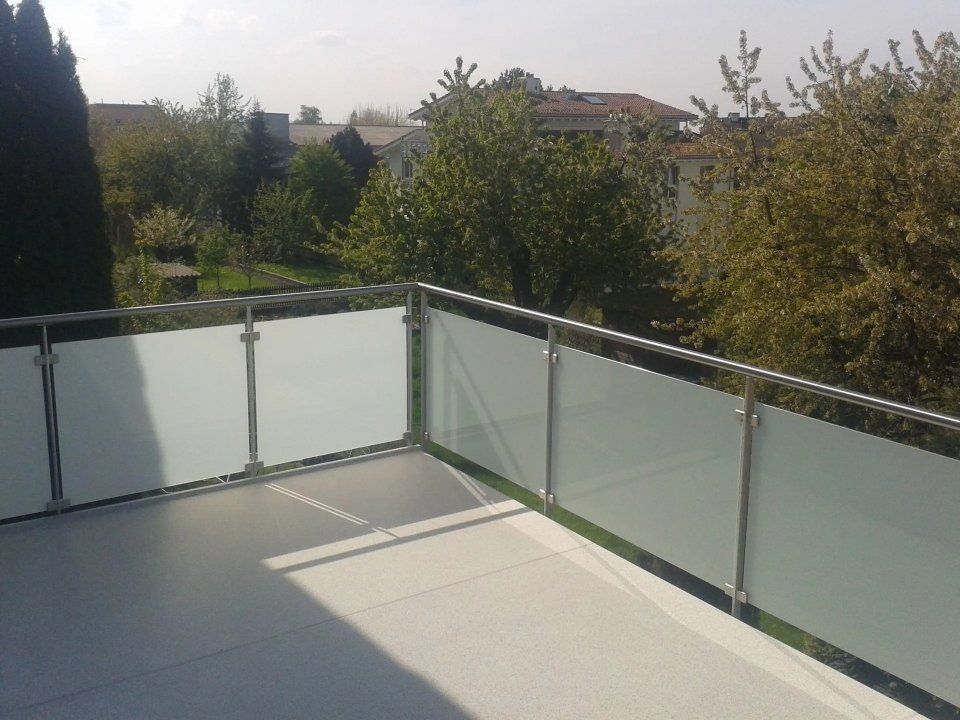 Sonnendurchfluteter Balkon mit Milchglasgeländer und Blick auf Bäume und Häuser in der Ferne.