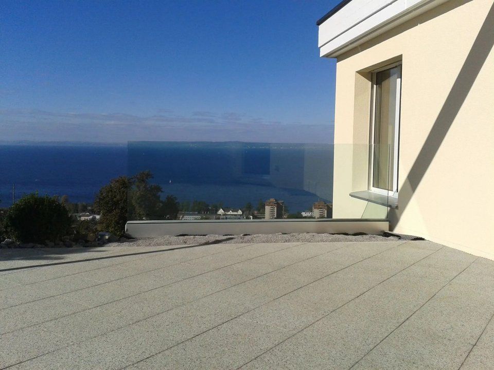 Dachterrasse mit Glasgeländer und Blick auf das Meer und den blauen Himmel neben einem cremefarbenen Gebäude