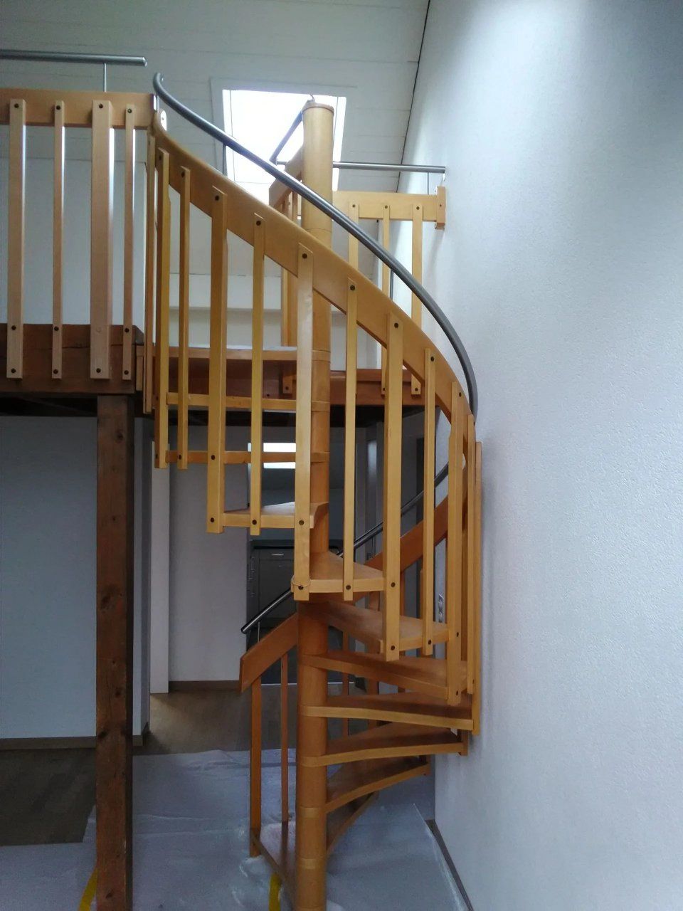 Geschwungene hölzerne Wendeltreppe in einem Loft mit Geländer und Fensterlicht