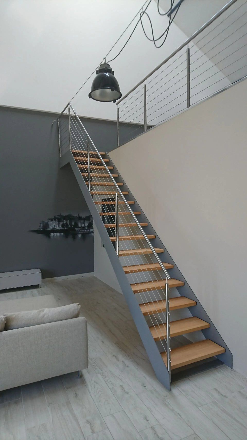 Moderne Innentreppe mit grauem Metallgeländer, Holzstufen und einer schwarzen Hängeleuchte in einem Loft-Zimmer