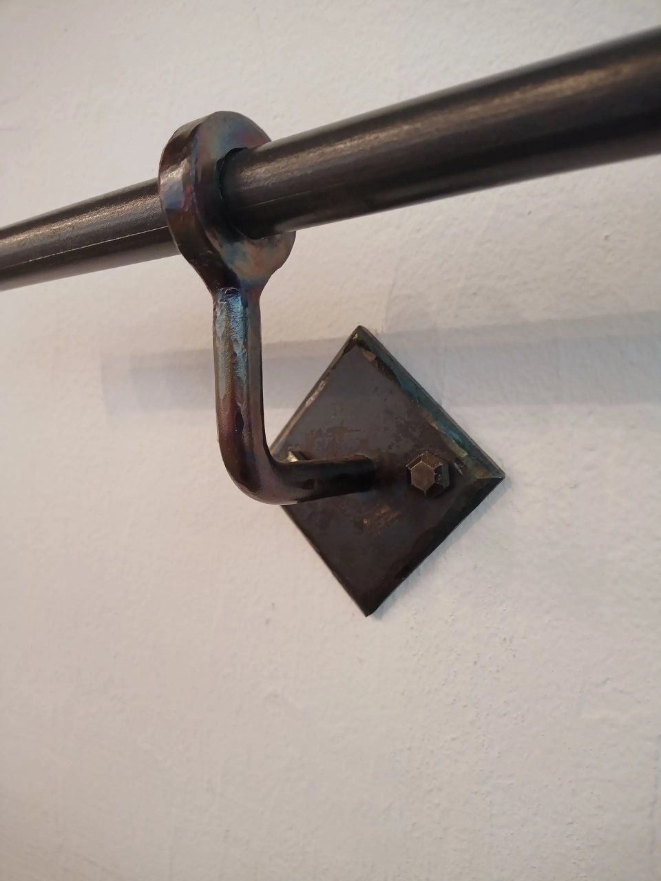 Schwarze Metall-Gardinenstangenhalterung an einer weissen Wand mit einer braunen Gardinenstange.