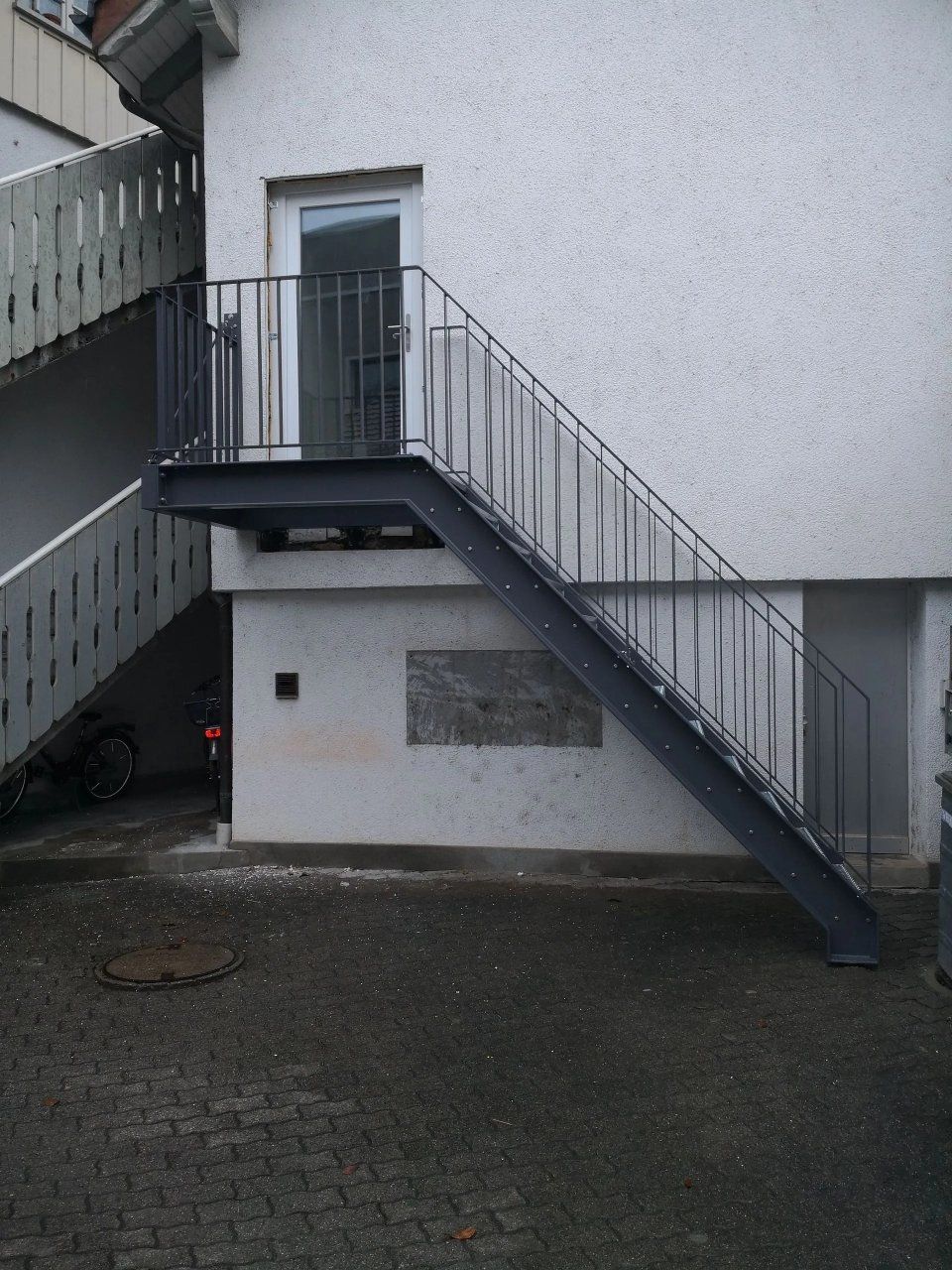 Eine Aussentreppe mit Metallgeländer führt zu einer weissen Tür an einer Gebäudewand.
