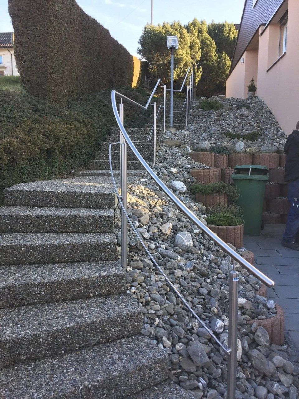 Steile Aussentreppe aus Beton mit Metallgeländer neben einem Kieshang und Wohnhäusern