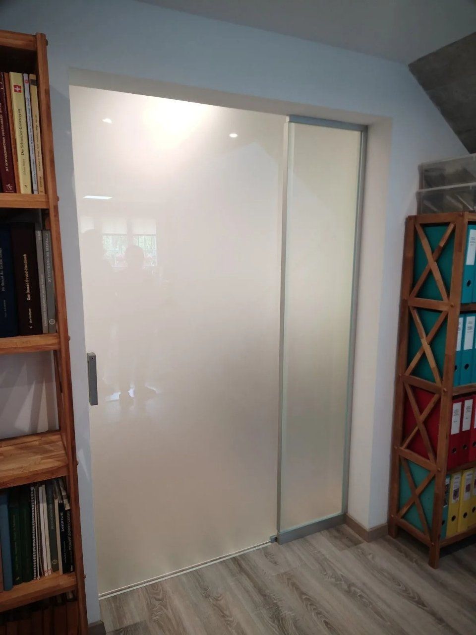 Weisse Schiebetüren für einen Kleiderschrank in einem Zimmer mit Bücherregalen auf beiden Seiten.