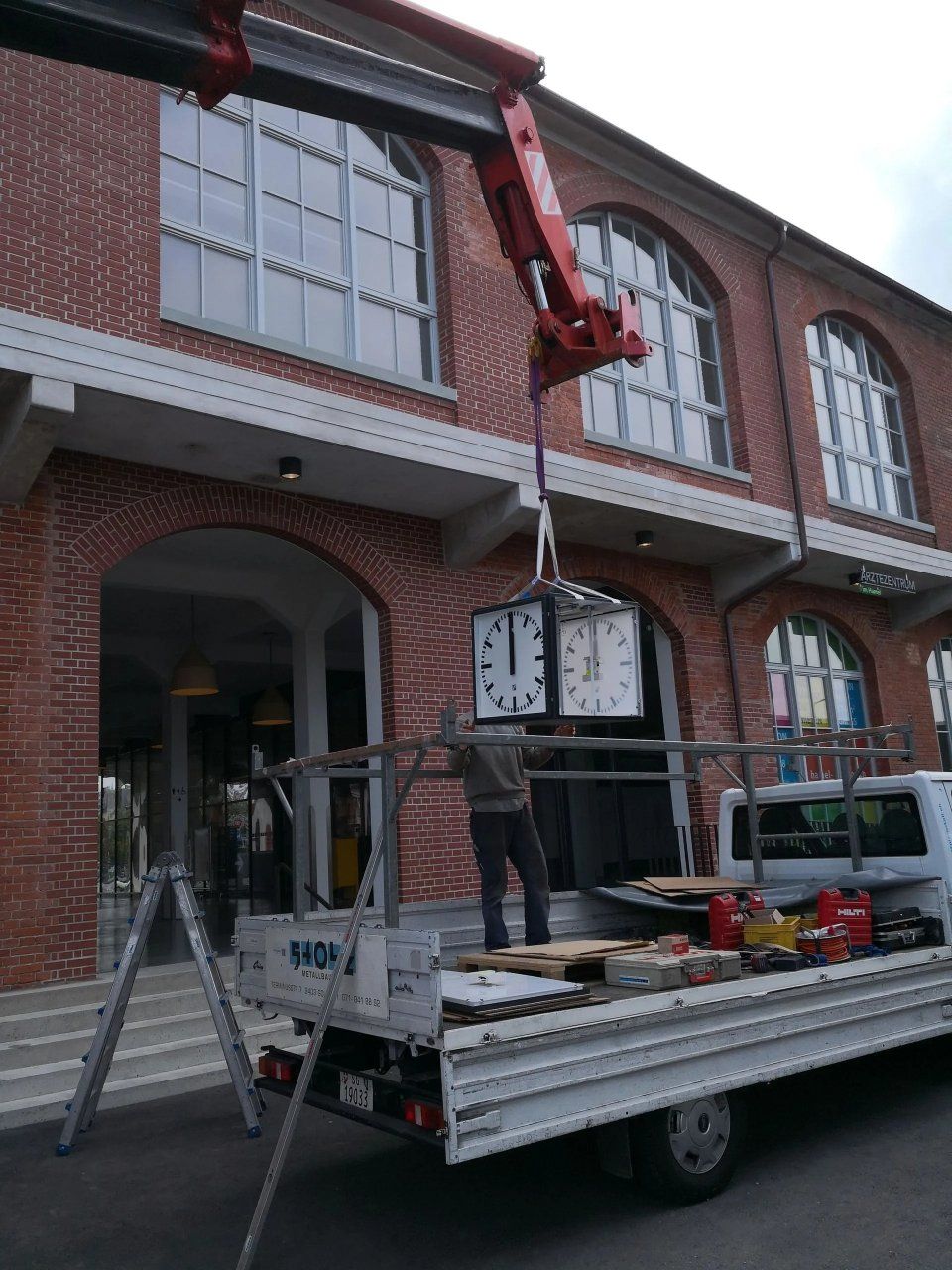 Ein Arbeiter hievt eine Hängelaterne von einem Pritschenwagen zur Aussenfassade eines Backsteingebäudes im zweiten Stock.