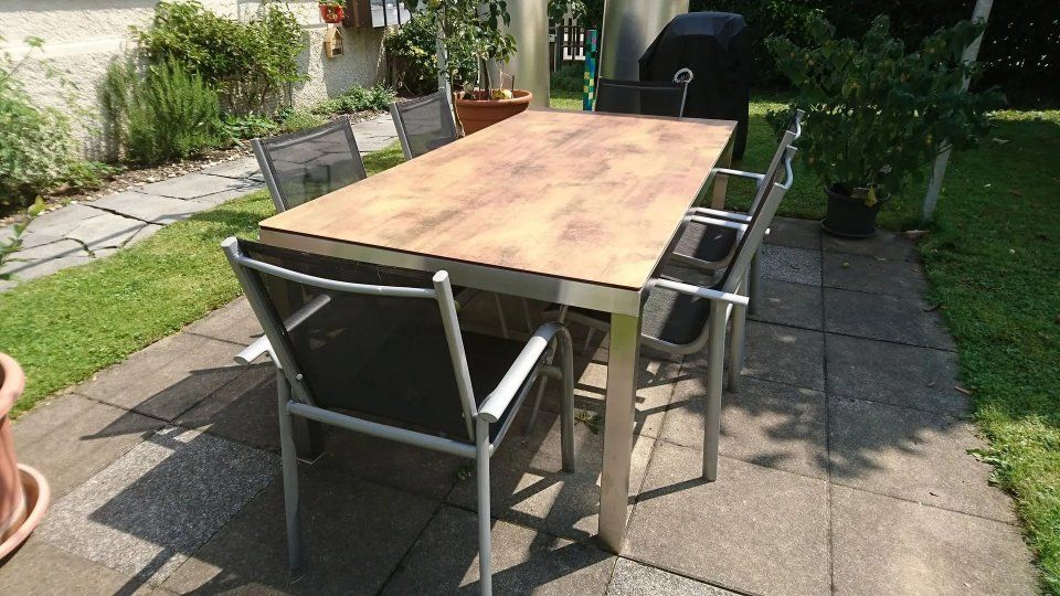 Esstisch im Freien mit vier Metallstühlen auf einer Steinterrasse neben einem Garten