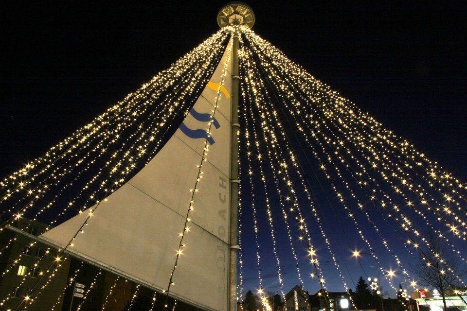 Ein nachts beleuchteter, segelförmiger Turm, übersät mit herabfliessenden goldenen Lichterketten.