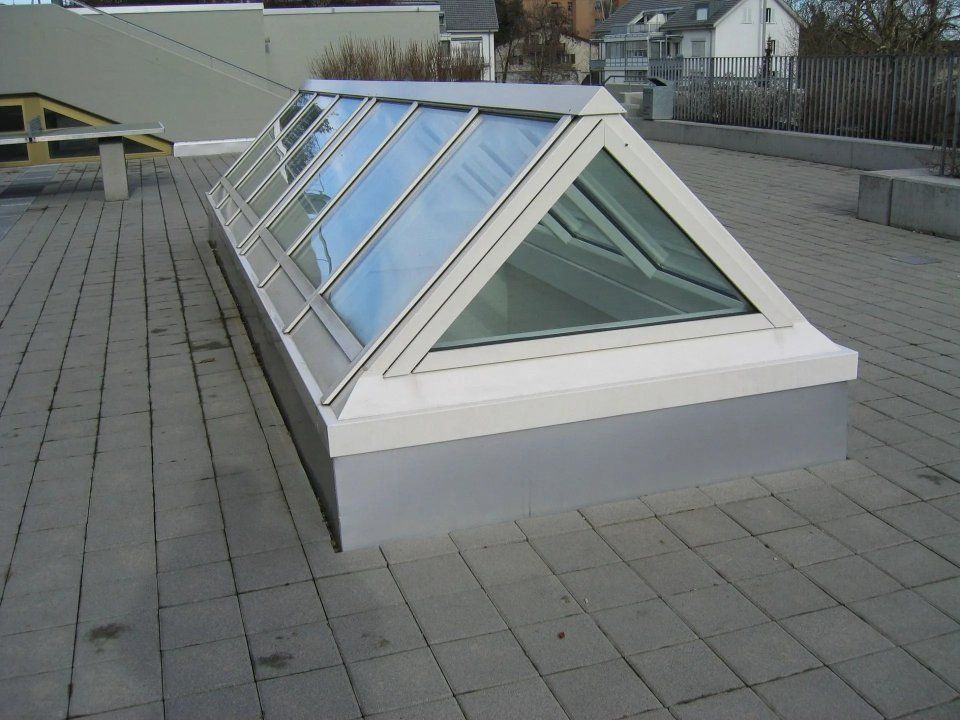 Glasoberlicht auf einem Flachdach mit weissem Rahmen und angrenzendem gefliestem Pflaster.