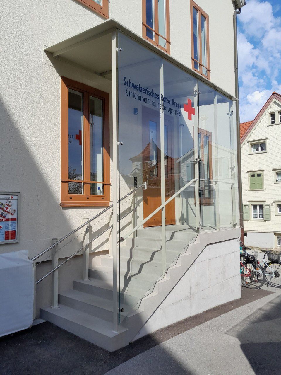 Verglaster Eingang mit Treppe und Handlauf an einem weissen Gebäude in einer engen Strasse