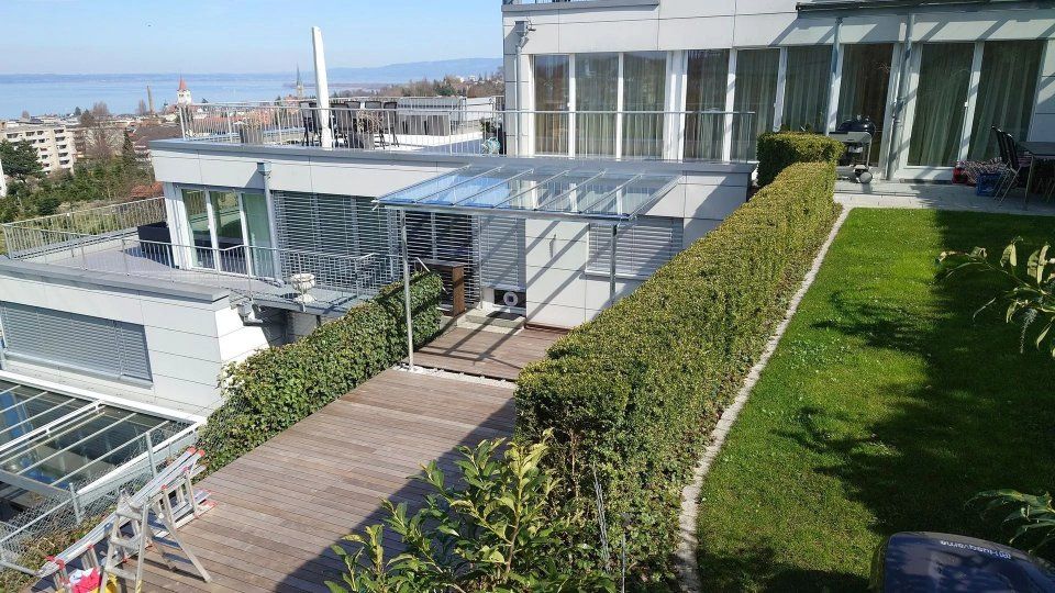 Ein begrünter Dachterrassenweg mit Glasdach, grünen Hecken und Blick auf die Skyline der Stadt im Hintergrund.