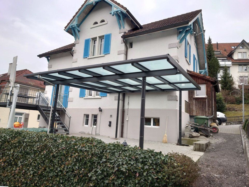 Haus mit gläsernem Carport und Hecke in einem Wohngebiet