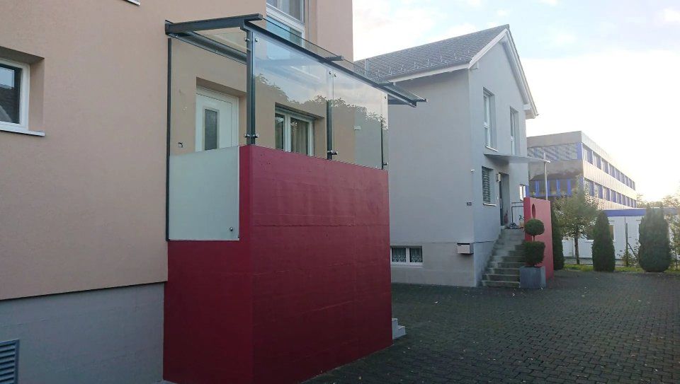 Moderner Wohnungshof mit roter Mauer und Glasbalkon neben einem gepflasterten Gehweg.