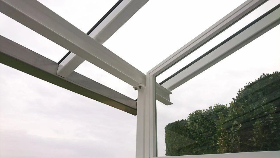 Blick durch das weissgerahmte Glasdach des Wintergartens auf den bewölkten Himmel und die Bäume
