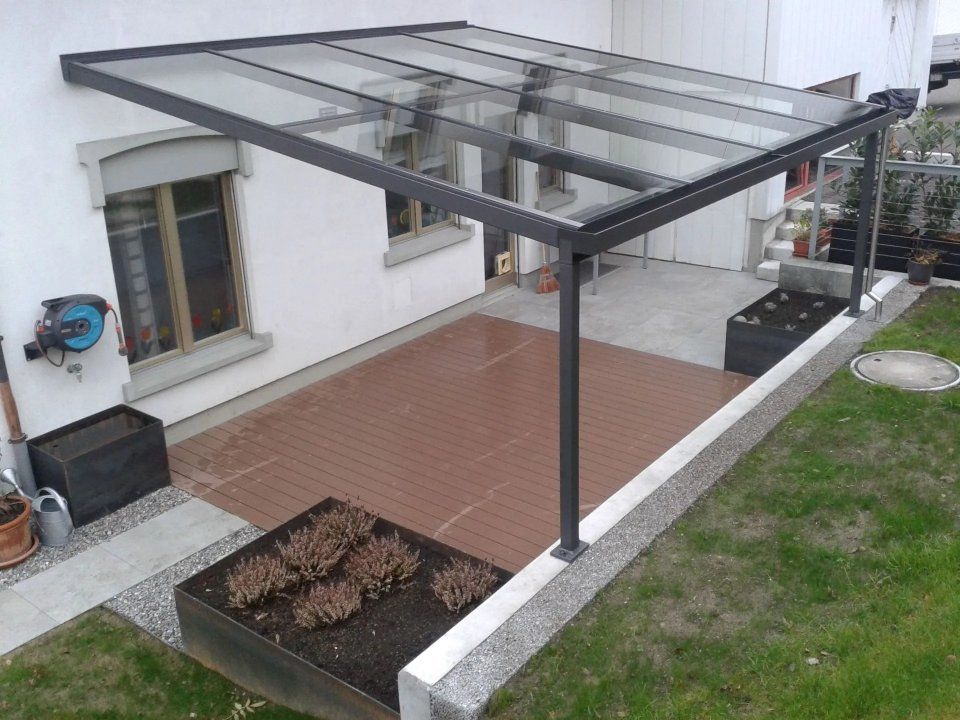 Überdachte Terrasse mit Glasdach über einer rot gefliesten Terrasse neben einem Haus und Garten