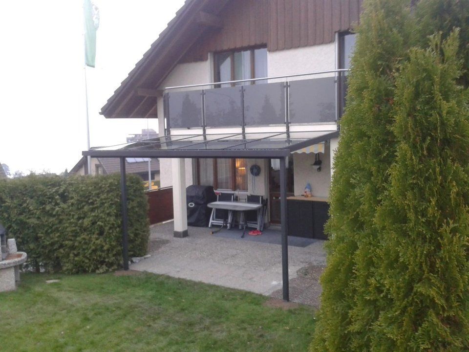 Terrasse im Hinterhof mit überdachter Pergola, Tisch und Stühlen, neben einem Haus und einer Hecke