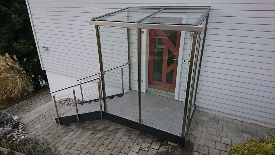 Überdachte Rollstuhlrampe und Eingangsplattform neben einem Gebäude mit roter Tür