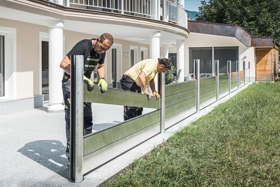 Zwei Arbeiter installieren einen gläsernen Terrassenzaun neben einem modernen Haus
