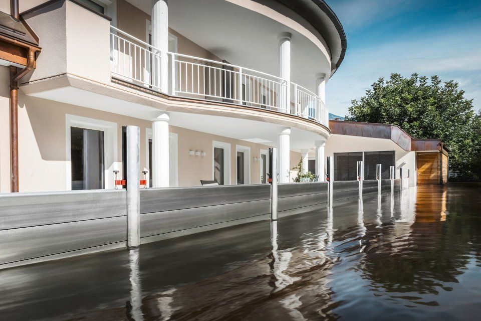 Hochwasser umgibt ein weisses Haus mit geschwungenen Balkonen und einem hölzernen, dockähnlichen Steg.