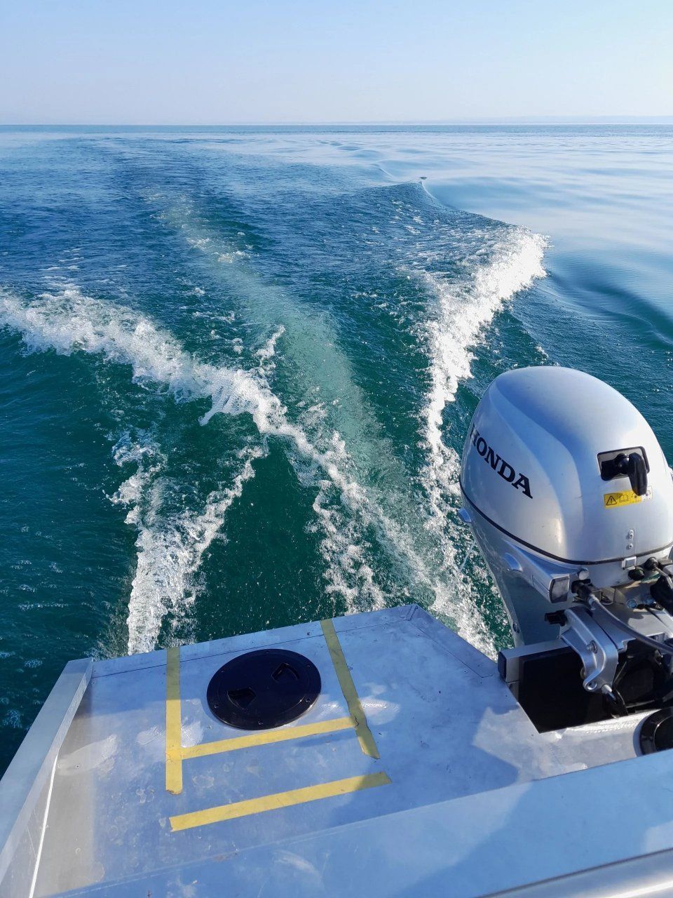 Blick vom Heck eines Bootes, dessen Honda-Motor über das blaue Wasser gleitet und eine schäumende Kielwasserwelle hinterlässt.