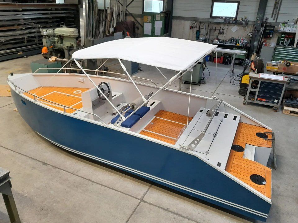 Blau-weisses Motorboot mit Verdeck, vor Anker in einer Werkstatt.