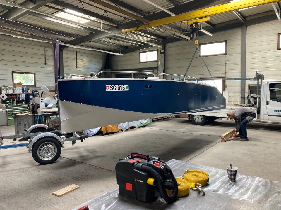 Ein blaues und graues Boot auf einem Anhänger in einer Werkstatt, in deren Nähe sich Werkzeuge und Ausrüstung befinden.