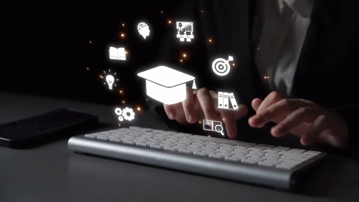 Persona escribiendo en un teclado con iconos educativos flotantes, incluyendo un birrete de graduación.